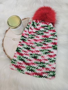 a knitted hat with a red pom - pom sits next to a cup of coffee