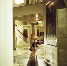 two people are walking down the hall in an elegant house, one is talking on her cell phone