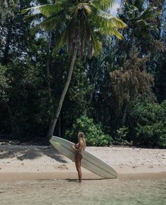 a woman holding a surfboard on top of a sandy beach