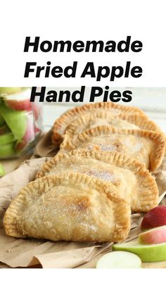 three apple hand pies sitting on top of brown paper next to sliced apples and a jar of water