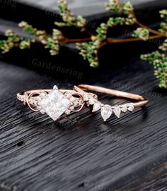 two rose cut diamond engagement rings on top of a wooden table with greenery in the background