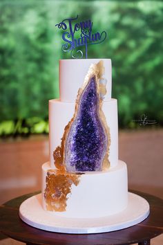 a three tiered cake with purple and gold decorations on the top is decorated with an amethyst