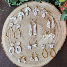 an assortment of earrings sitting on top of a wooden table next to flowers and greenery