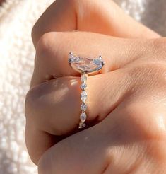 a woman's hand holding a ring with an oval shaped diamond on top and small round diamonds around the band