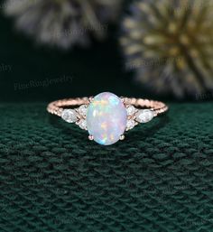 a white opal and diamond ring sitting on top of a green surface with flowers in the background