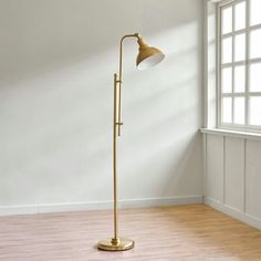 a floor lamp in an empty room with white walls and wooden floors, near a window