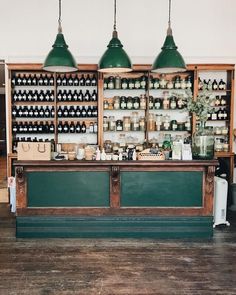 an old fashioned bar with three green lights hanging from it's ceiling and bottles on the shelves