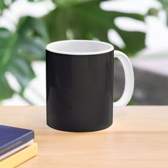 a black and white coffee mug sitting on top of a wooden table next to a book