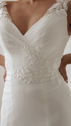 a woman wearing a white wedding dress with flowers on the waist and sleeves, holding her hands behind her back