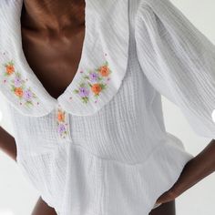 a woman wearing a white top with flowers on it's chest and collared neckline