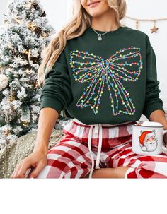 a woman sitting on a couch wearing a green christmas sweater and plaid pants with lights all over it