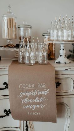 a cookie bar sign on top of a table with empty glasses and candy bars in the background