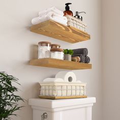 two wooden shelves above a toilet with towels and other items on it in a bathroom