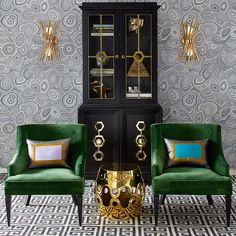 two green chairs sitting next to each other in front of a black cabinet with gold accents