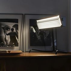 a desk lamp sitting on top of a wooden table next to an open book and some pictures