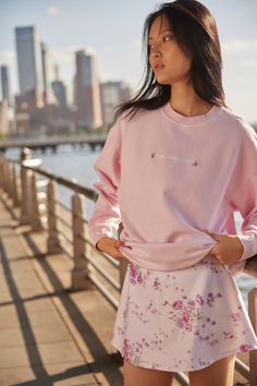 a woman standing on a bridge next to the water wearing a pink sweatshirt and floral skirt