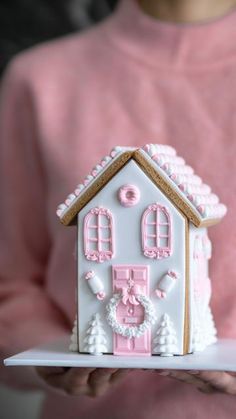 a woman holding a white and pink house shaped cake on top of a paper plate