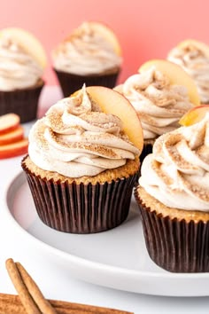 cupcakes with frosting and apples on a white plate next to cinnamon sticks