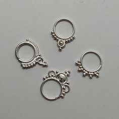 three pairs of silver colored nose rings on a white surface