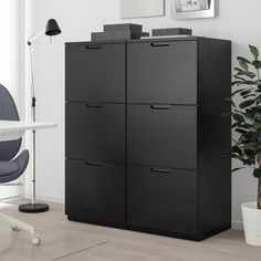 a black cabinet sitting next to a chair in a room with a potted plant