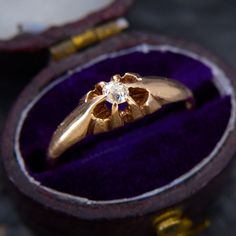 a gold ring with a diamond in it sits inside a purple velvet box on the ground