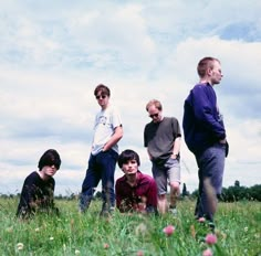 four young men standing in the grass with one sitting on the ground looking at something