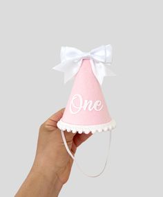 Bow party hat is made of - pink merino felt - white bow front and back - white iron on One - white pompom trim - elastic band Size is  H 12 cm W 8 cm IMPORTANT: Please do not give it to the baby or kids to play with. It can cause choking due to small particles or decorations. So please take that granted. THANK YOU Kindly note: Make sure your address is correct during checkout to avoid product loss If you want your party hat ASAP, choose "Rush my order" under quantity section in order to be made and shipped within 24 hour. Returns and Exchanges are accepted ✅Check policy With Love, Elina Whimsical White Mini Hat As Gift, Whimsical White Mini Hat For Gifts, Cute White Hat For First Birthday, Cute White Hat With Bow, Cute White Hats With Bow, Playful White Party Supplies, Playful White Party Hat, Cute White Party Supplies For Gifts, Cute White Party Supplies For Gift