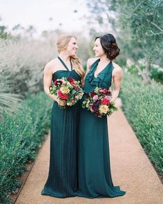 two women in green dresses standing next to each other on a path with greenery