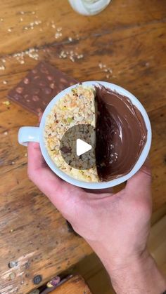 a person holding a cup with a chocolate cake in it on top of a wooden table