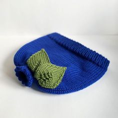 a blue knitted hat with a green leaf on the front and bottom, sitting on a white surface