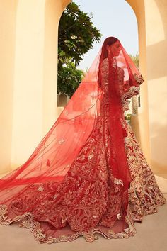 a woman wearing a red bridal gown and veil standing in front of an archway