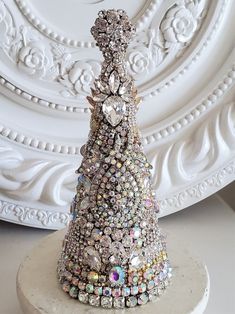 a christmas tree made out of jewels on a white pedestal in front of a wall