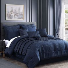 a bed with blue comforters and pillows in a room next to a large window