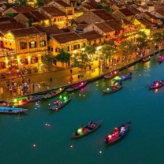 boats are floating on the water in front of buildings and lights at night, with people walking around them