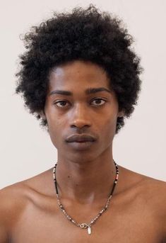 a young man with an afro wearing a beaded necklace and looking at the camera