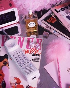 an assortment of electronic devices and magazines on a table with pink feathery decorations around them