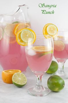 three glasses filled with pink lemonade next to limes and oranges on a table