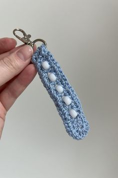 a hand holding a crocheted keychain with white buttons on the end