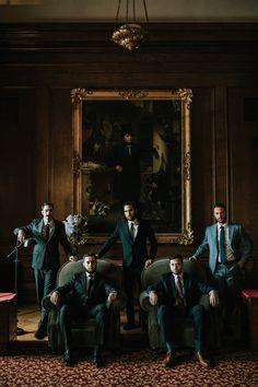 four men in suits and ties posing for a photo with a large painting behind them