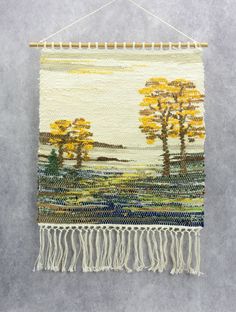 a tapestry hanging on a wall with yellow trees in the background and blue water below