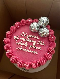 a birthday cake with pink frosting and two disco balls on top, in a box