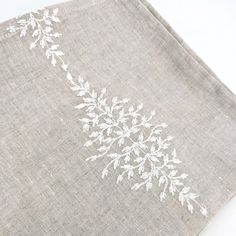 a close up of a table cloth with white flowers and leaves on grey linens