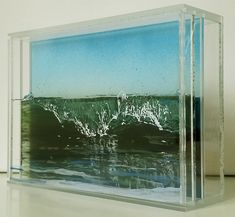 a glass block with water and waves in the ocean on it's sides, against a white wall