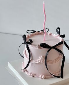 a pink cake with black ribbons and a single candle