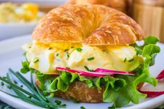 a croissant sandwich with eggs and cheese on it sitting on a white plate