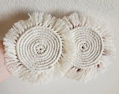 two white round rugs with tasselled ends on a handmade wall hanging