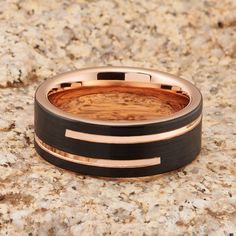 a wedding band with black and rose gold inlays sits on a marble surface