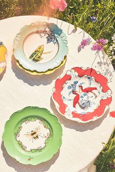 three plates sitting on top of a white table covered in green and red flowers next to each other