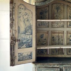 an old wooden cabinet is painted with blue and white floral designs on the doors, which are open