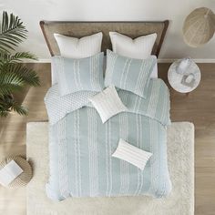 a bed with blue and white comforters on top of it next to a potted plant